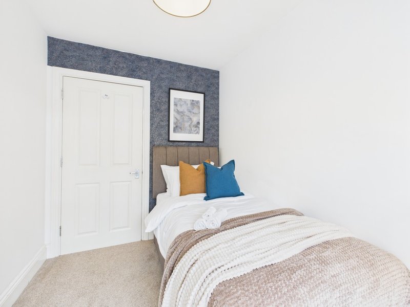 Bedroom with single bed, blue headboard, colorful pillows and white wardrobe