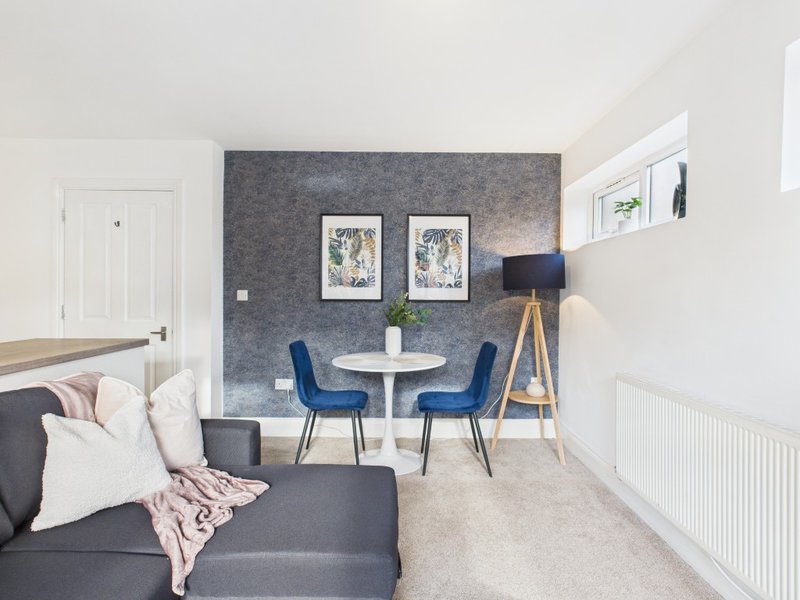 Modern living room with gray sofa, round white table, blue chairs and feature wall