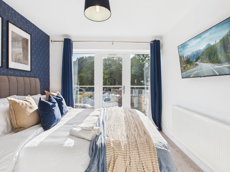 Modern bedroom with double bed, blue headboard, patio doors overlooking balcony and landscape