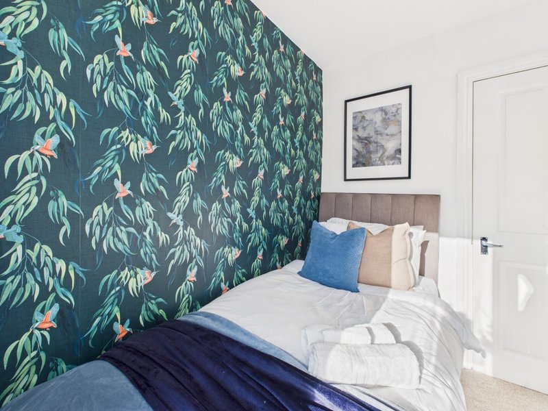 Modern bedroom with botanical wallpaper, double bed with blue and cream pillows, and framed wall art
