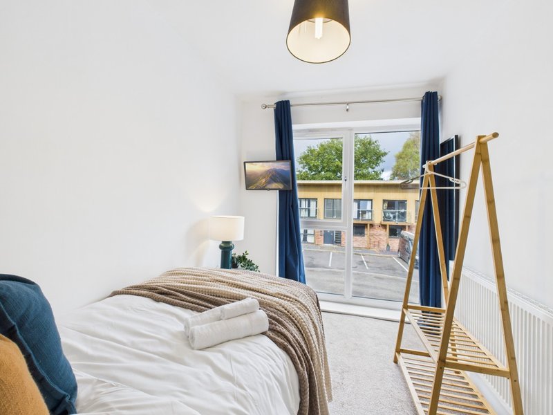 Bright bedroom with single bed, wooden coat stand, pendant lamp and window overlooking street