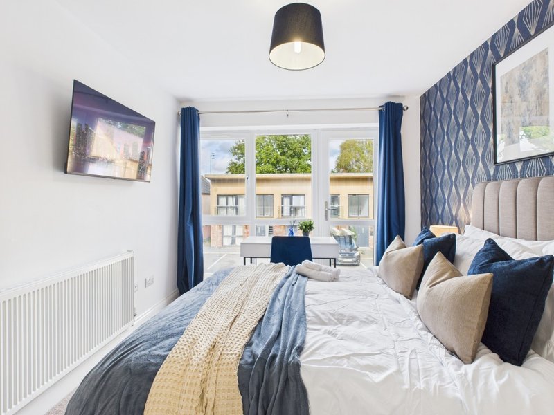 Modern bedroom with double bed, blue curtains, patterned wallpaper and street view windows