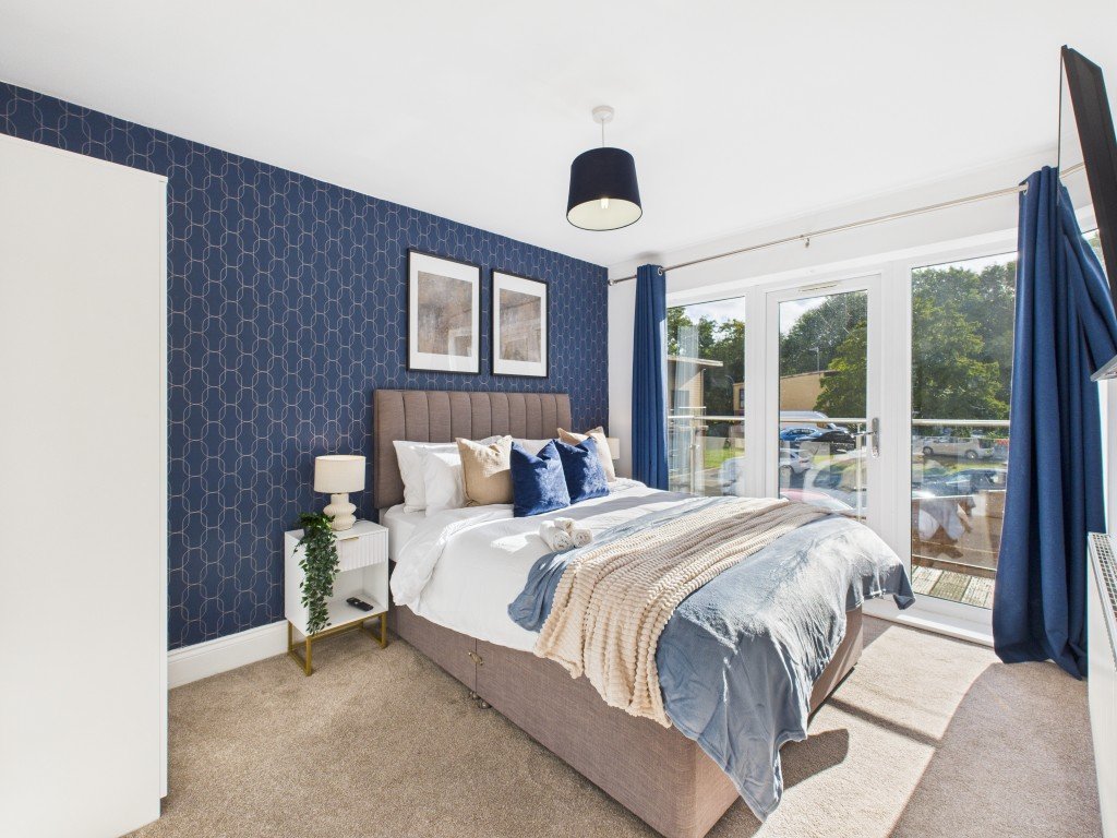 Modern bedroom with double bed, navy patterned wallpaper, large windows overlooking water and greenery