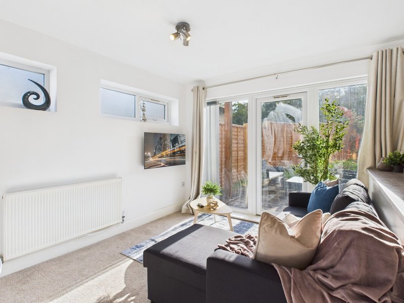 Bright living room with black sofa, brown throw blanket, and garden views through patio doors