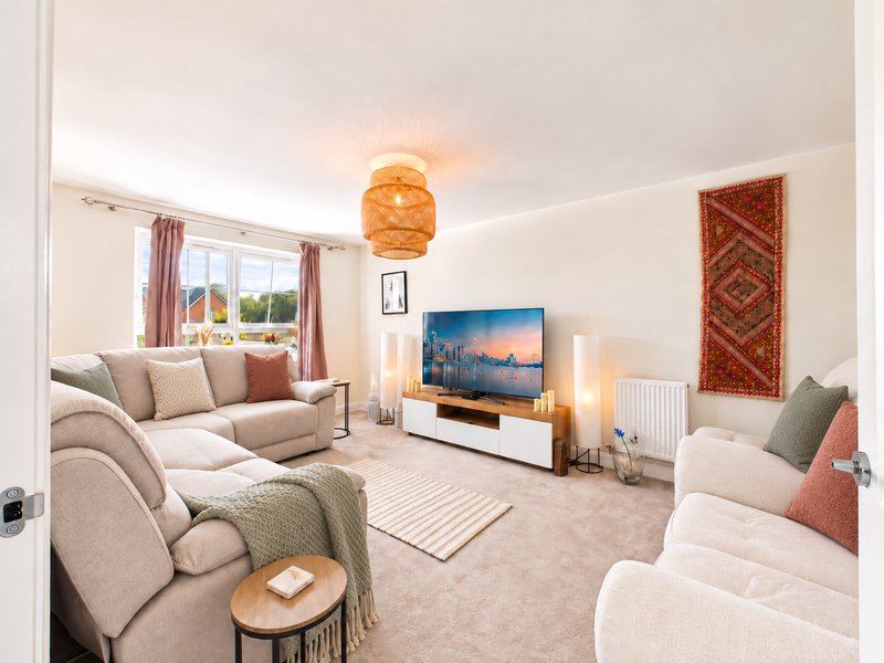 Spacious living room with two cream armchairs, beige sofa, TV, and orange pendant light