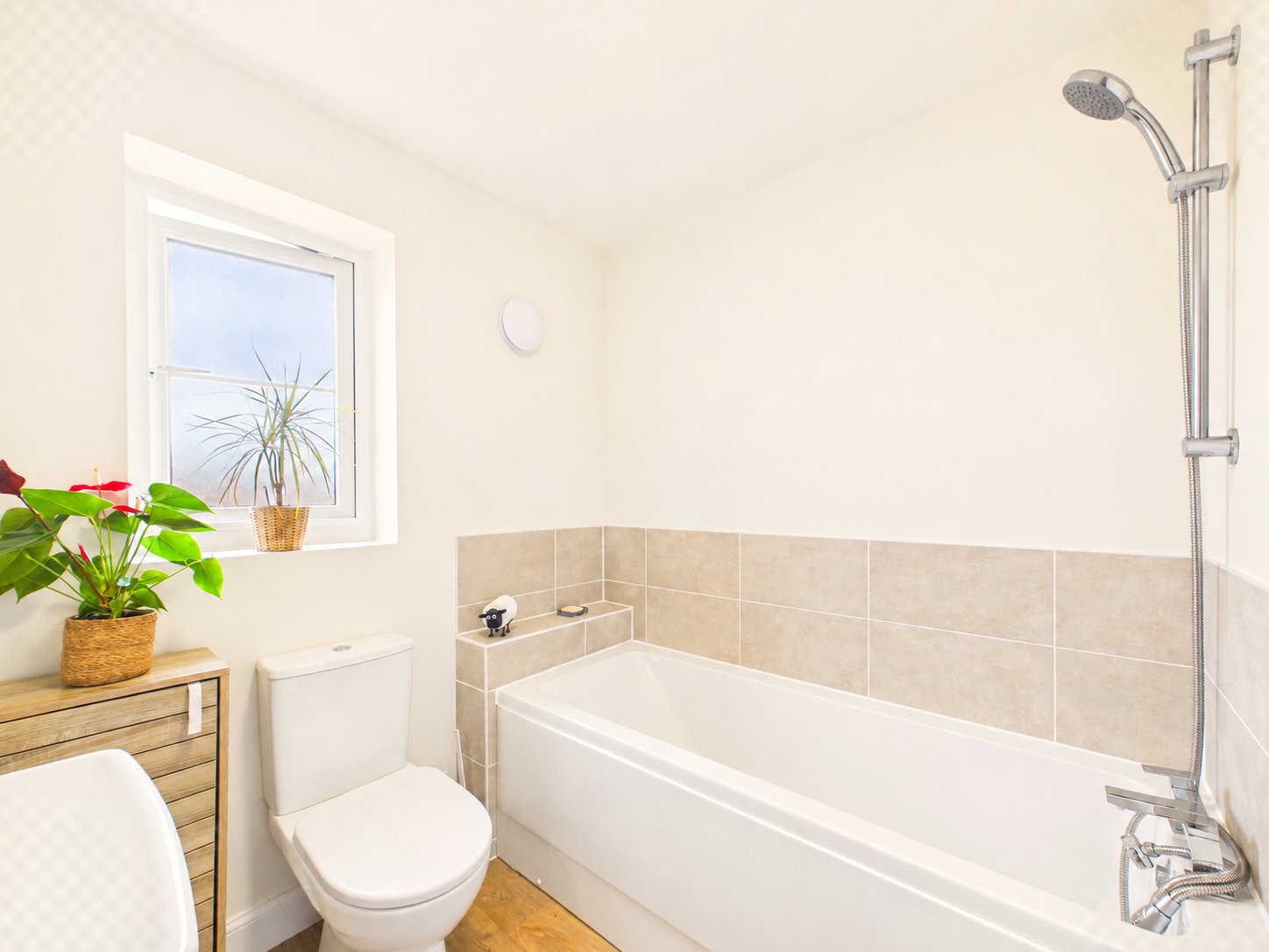 Bathroom with white toilet, bathtub, tiled wall, window, potted plant and shower fixtures