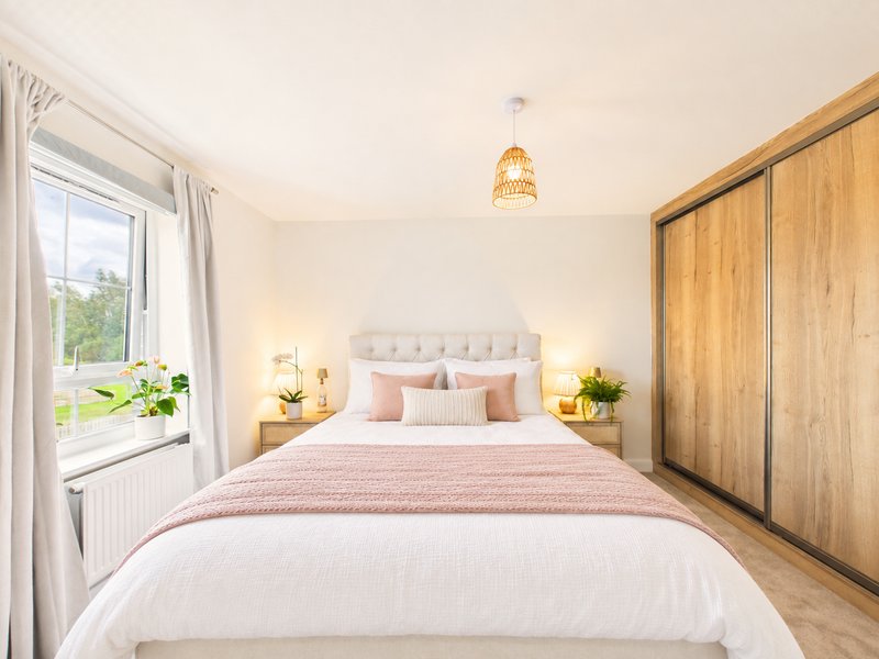 Bright bedroom with double bed, wooden wardrobe, bedside lamps and window with garden view