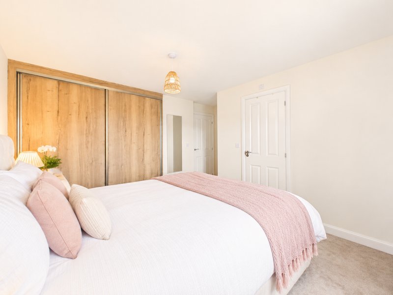 Bright bedroom with double bed, wooden wardrobe, pink bedding, and white doors