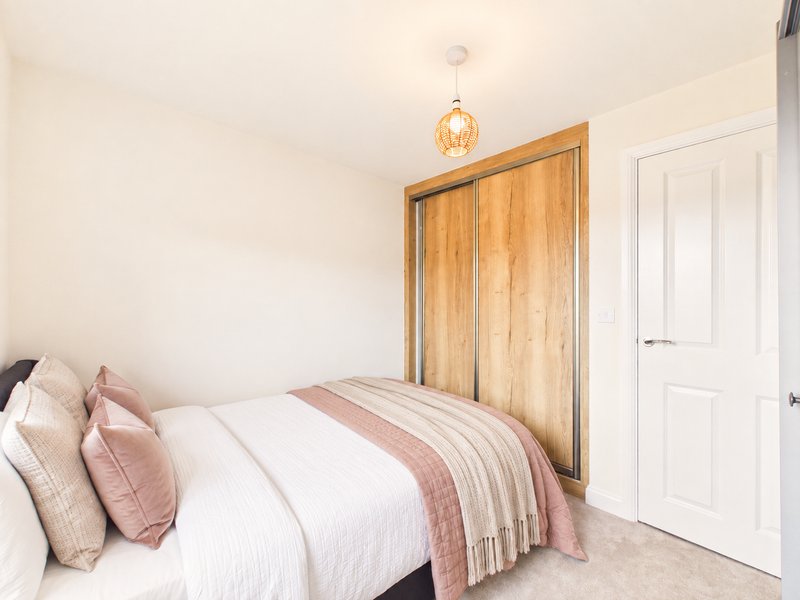 Bedroom with double bed, pink bedding, wooden wardrobe and pendant light