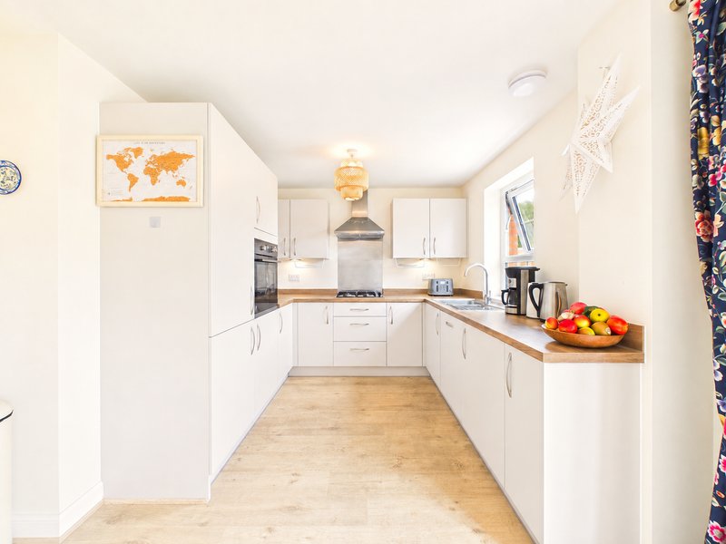 Modern white kitchen with wooden countertops, gas hob, and fruit bowl on island