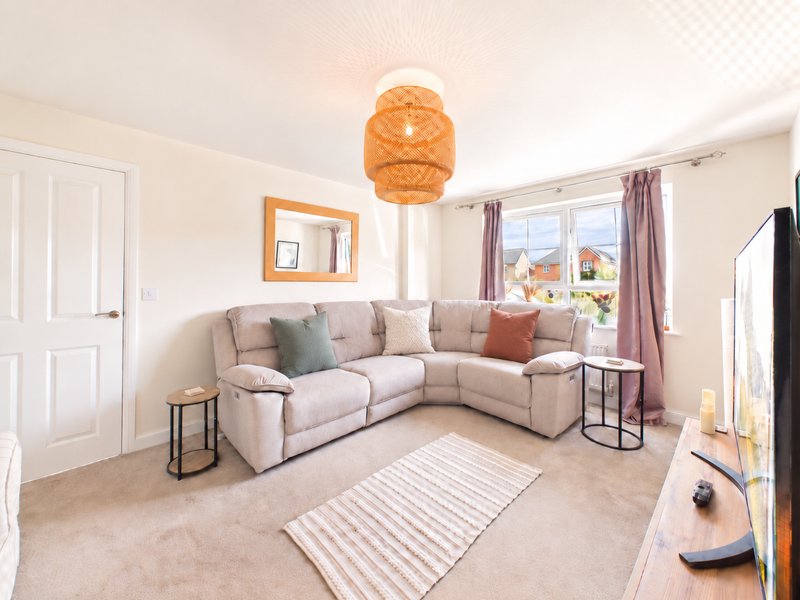 Bright living room with beige corner sofa, orange pendant lamp, striped rug and bay windows