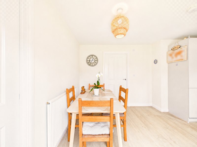 Dining area with wooden table, orange chairs, woven pendant light and clock