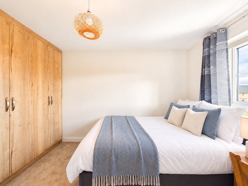 Bright bedroom with double bed, wooden wardrobe, woven pendant light and window
