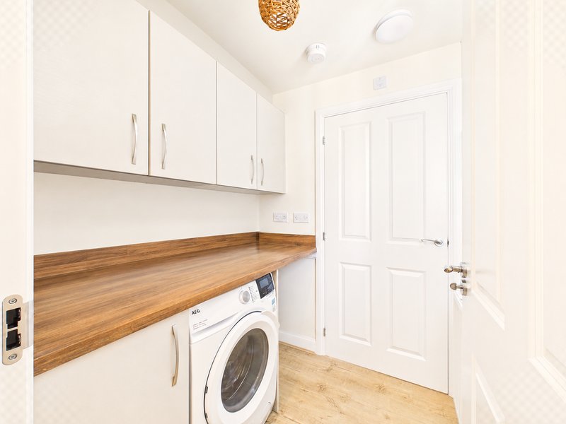 Modern utility room with white cabinets, wooden countertop, washing machine and door