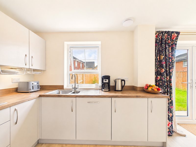 Modern kitchen with cream cabinets, wooden worktop, sink, and garden view through window