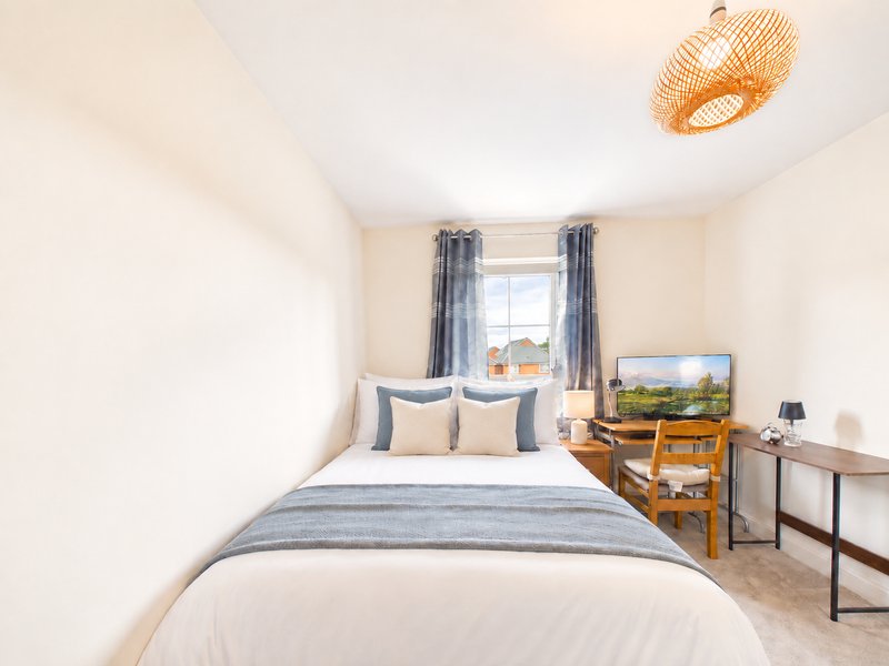 Bright bedroom with double bed, blue bedding, wooden furniture, window with curtains and wicker ceiling light