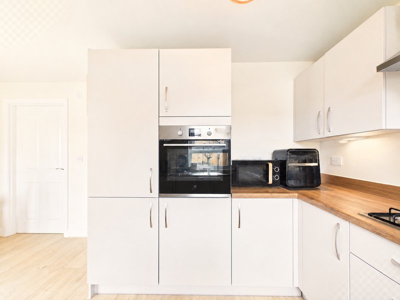 Modern white kitchen with wooden countertops, built-in oven, and stainless steel appliances