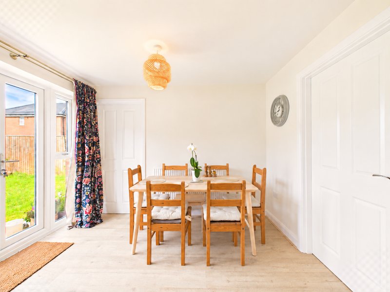 Bright dining room with wooden table, four chairs, pendant lamp and patio doors