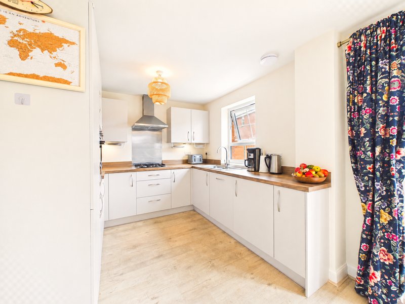Modern white kitchen with wooden worktops, gas hob, and floral curtains