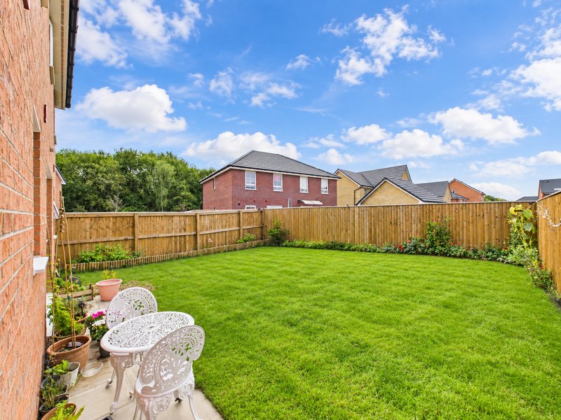 Spacious green garden with wooden fence, patio area, and brick house in background