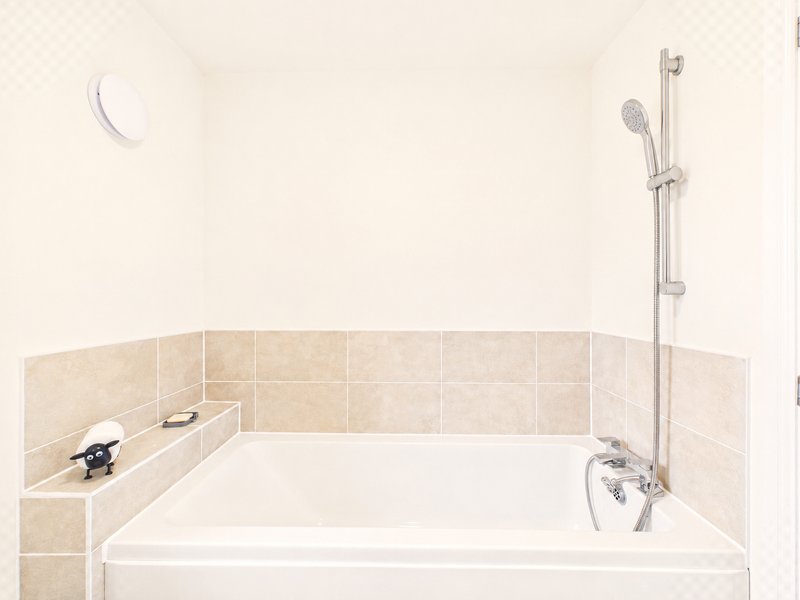 Bathroom with white bathtub, beige tile surround, and chrome shower fixtures