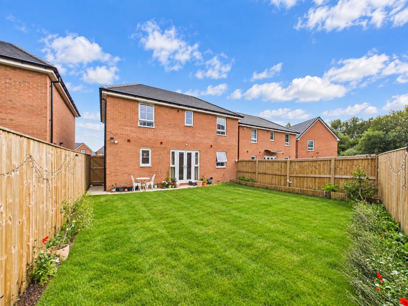 Rear garden view of brick residential property with lawn, wooden fencing and patio area
