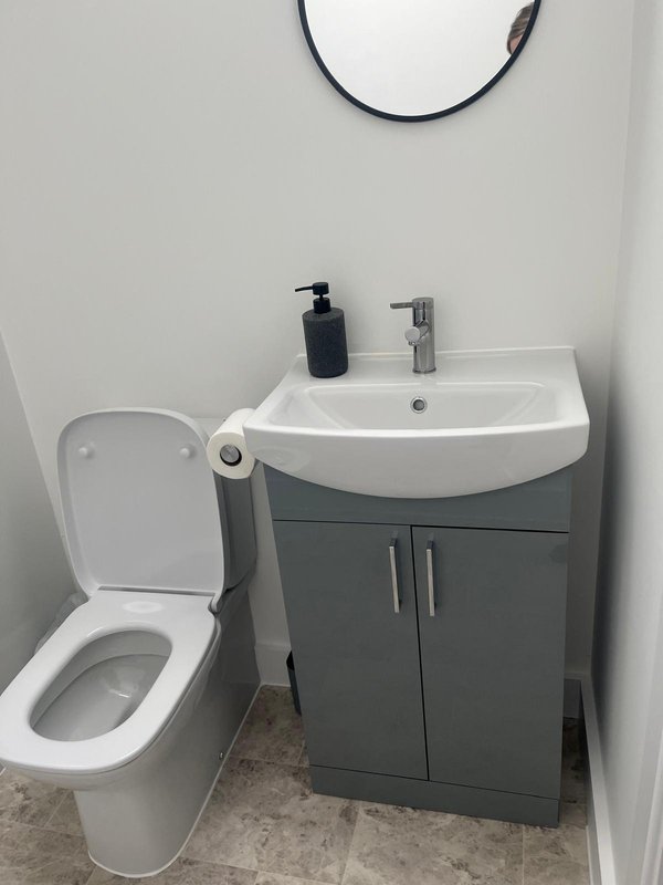 Modern bathroom with white toilet, grey vanity unit, curved white sink and round mirror