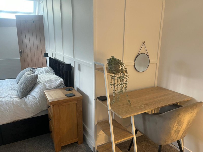 Bedroom with double bed, wooden nightstand, desk, hanging mirror, and potted plant