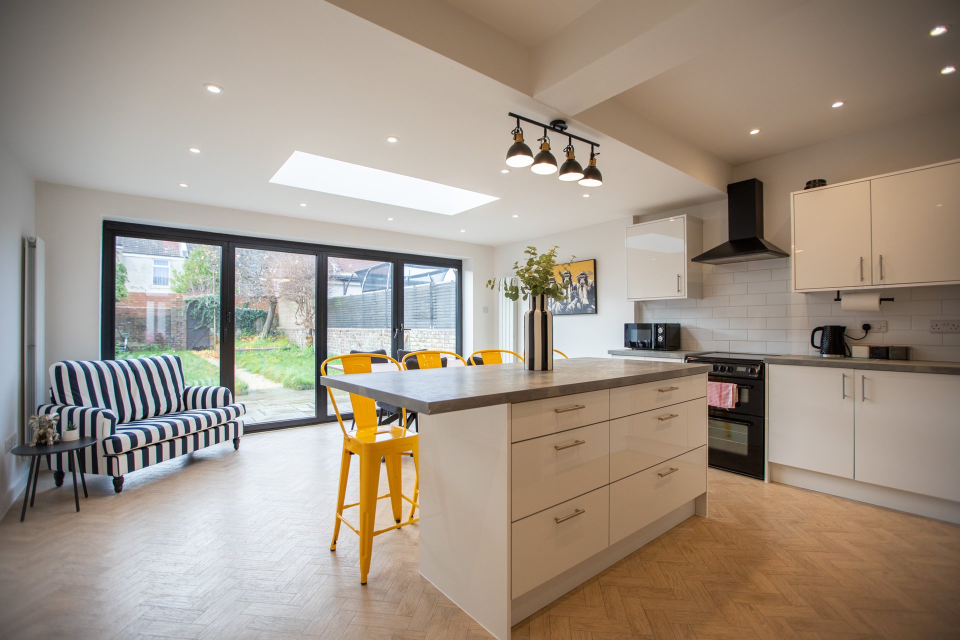 Modern open-plan kitchen and dining area with cream cabinetry, island seating, and garden views through patio doors