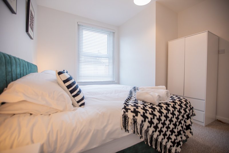Bright bedroom with double bed, green headboard, wardrobe, and window with blinds