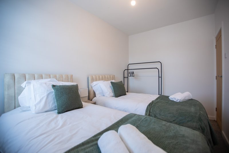 Bright bedroom with two single beds, green blankets, white pillows and neutral headboards