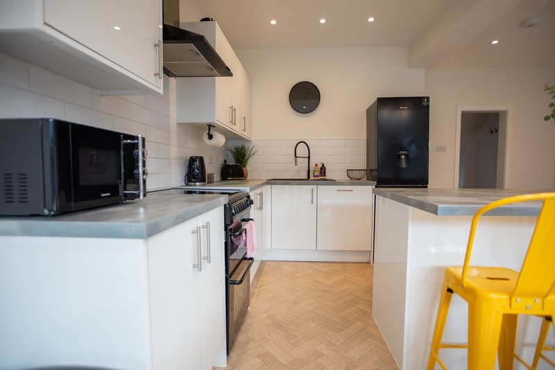 Modern kitchen with white cabinets, black appliances, herringbone flooring and yellow bar stool