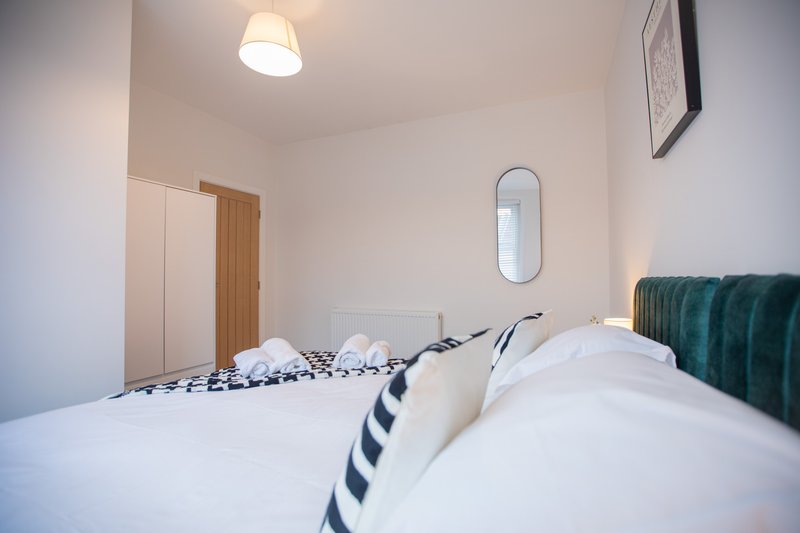 Bright bedroom with double bed, teal headboard, white bedding and ceiling light