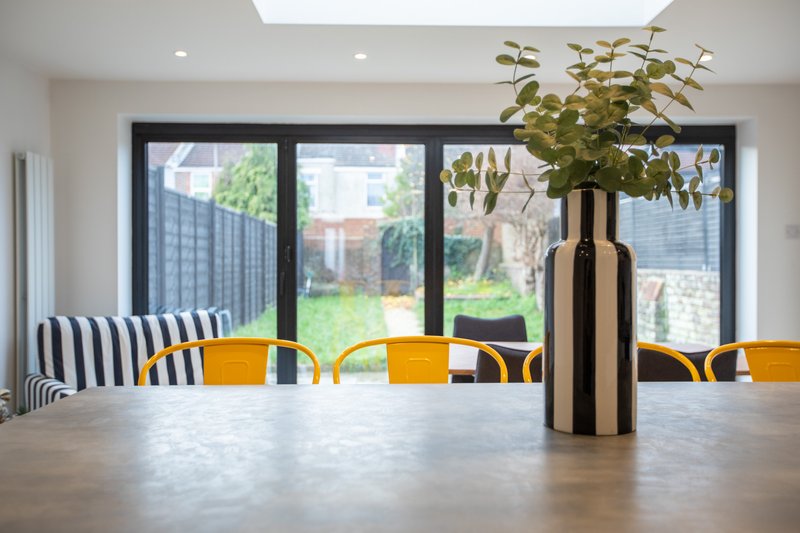 Modern dining room with large windows, wooden table, yellow chairs, and potted plant decoration