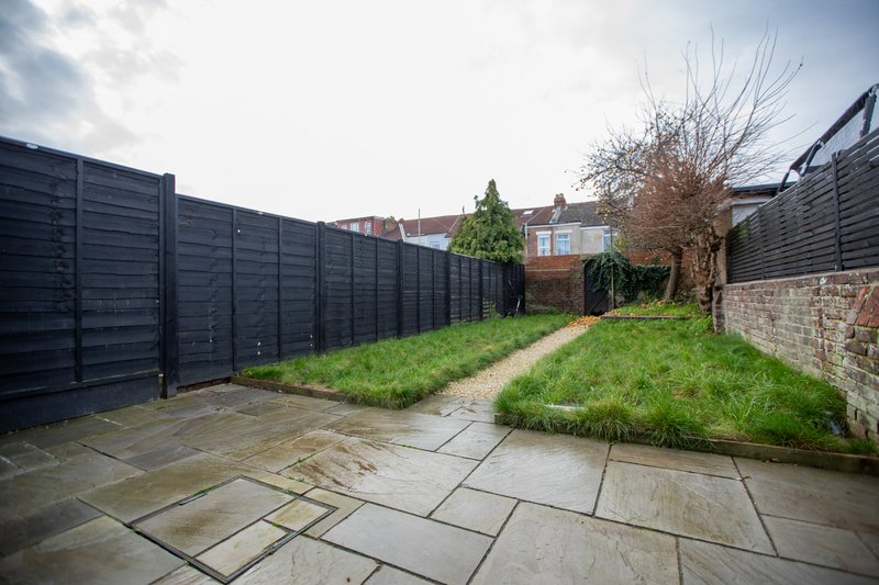 Rear garden with paved patio, lawn, black fencing and brick house beyond