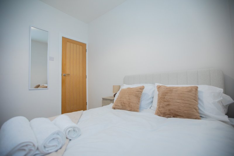 Bright bedroom with white bed, tan cushions, wooden door and small mirror
