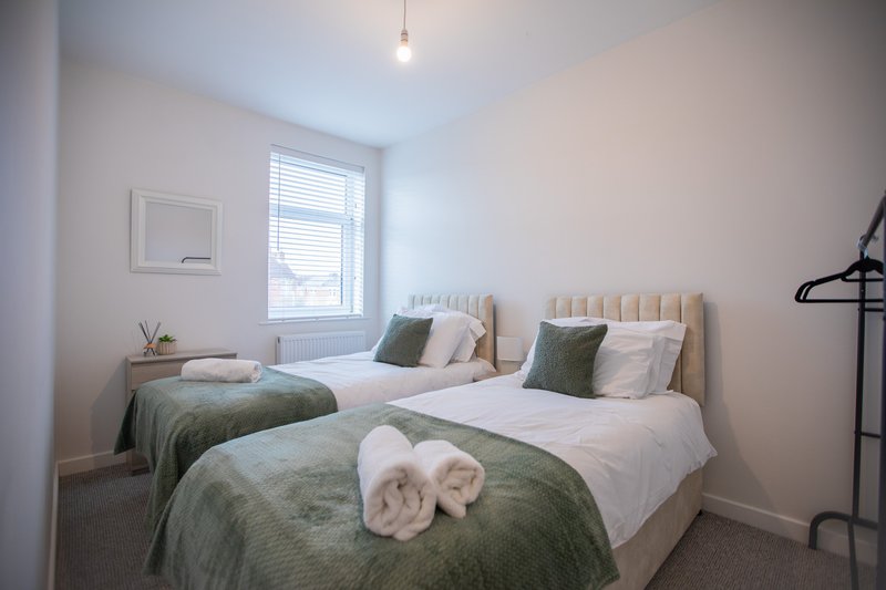 Twin bedroom with two beds, green bedding, white pillows, window with blinds, and hanging light fixture