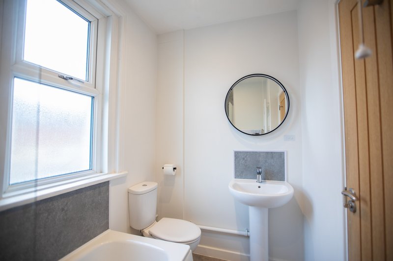 Clean bathroom with toilet, pedestal sink, round mirror and large window