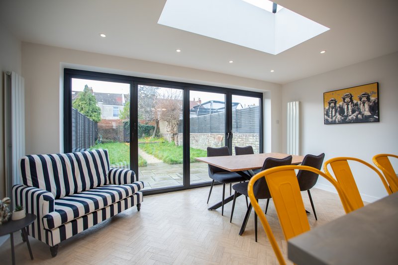 Modern open-plan living area with striped armchair, dining table, garden views and skylight