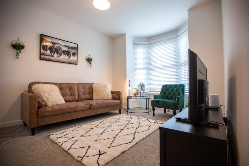 Living room with tan leather sofa, green armchair, TV, and geometric patterned rug