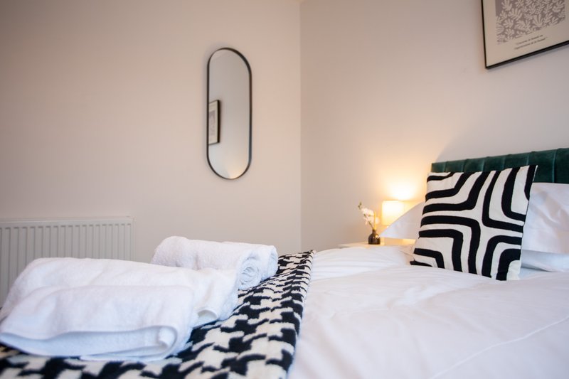 Modern bedroom with twin beds, white bedding, geometric patterned runner, and wall-mounted mirror