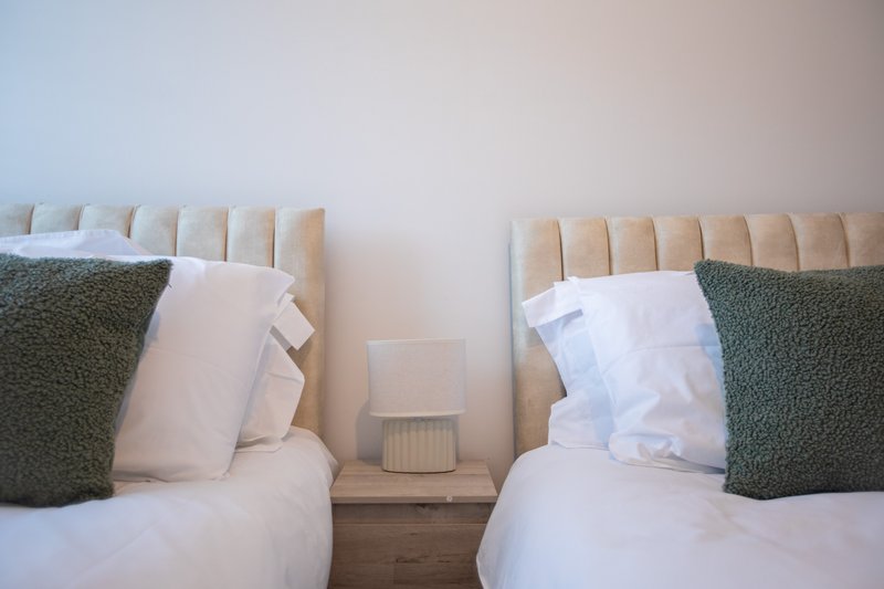 Twin beds with cream headboards, white bedding, green cushions and wooden nightstand between