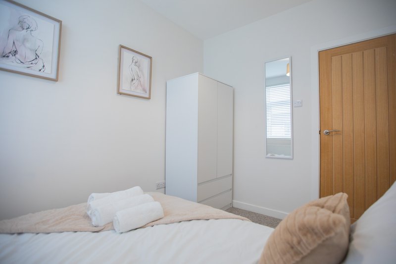 Bright bedroom with double bed, white bedding, wooden door, wardrobe and framed wall art