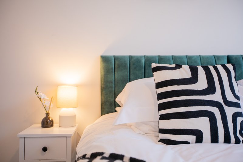 Modern bedroom with upholstered headboard, white bedding, geometric patterned pillows and bedside table