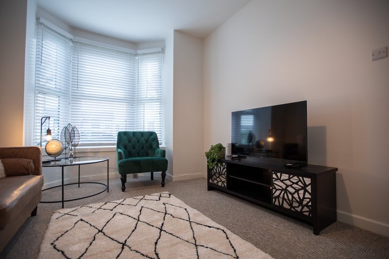 Modern living room with green armchair, TV stand, patterned rug and bay windows