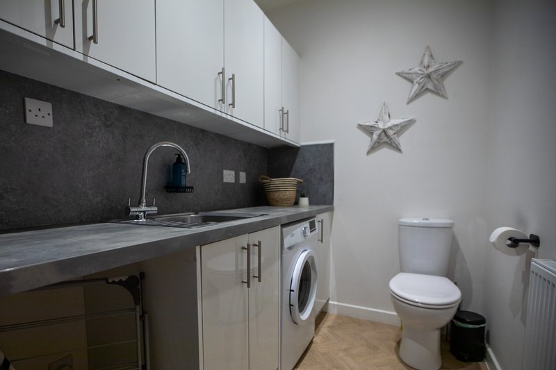 Utility room with white cabinetry, dark countertop, washing machine and toilet