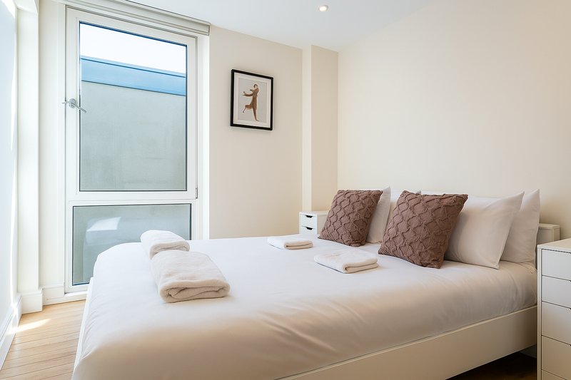 Modern bedroom with double bed, brown cushions, wooden floor and balcony door