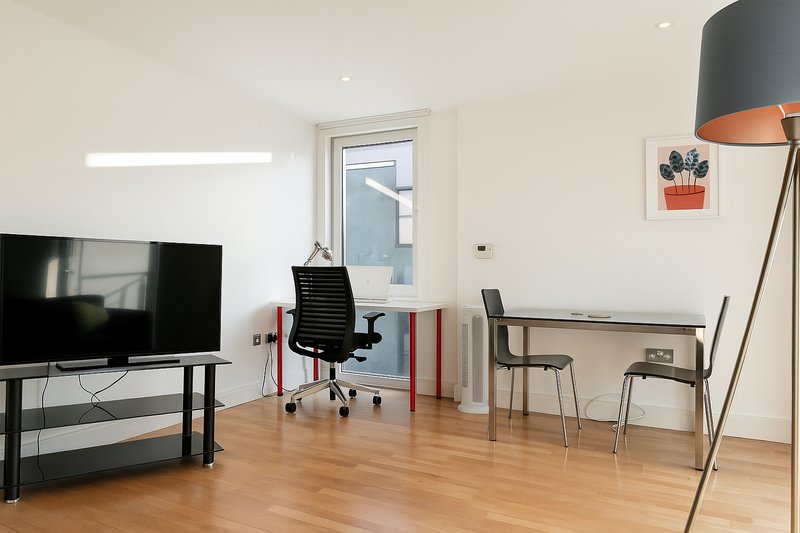 Modern open-plan living space with TV, desk chair, wooden flooring and floor lamp