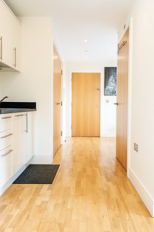 Bright kitchen corridor with white cabinetry, wooden flooring, and multiple doorways