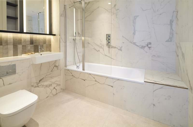 Modern bathroom with marble tiles, walk-in shower, toilet and illuminated mirror